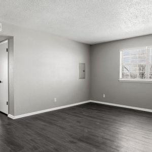 Empty renovated living room with dark wood flooring, gray walls, and a large window with blinds