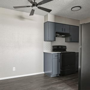 Renovated kitchen with blue cabinets, black appliances, subway tile backsplash, and adjoining open room with ceiling fan.