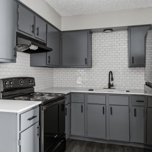 Renovated kitchen with gray cabinets, subway tile backsplash, black fixtures, and stainless steel refrigerator