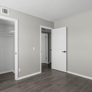 Empty bedroom in a renovated apartment with open closet, hardwood flooring, and hallway access