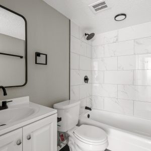 Renovated bathroom with white marble-tile tub surround, black fixtures, vanity sink, and toilet