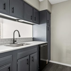 Renovated kitchen with dark gray cabinets, white countertops, subway tile backsplash, and stainless sink with black faucet.