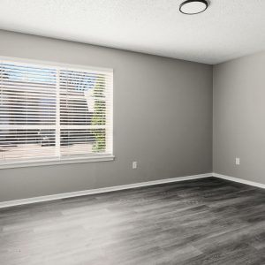 Empty renovated bedroom with gray walls, wood-style flooring, and a large window with blinds