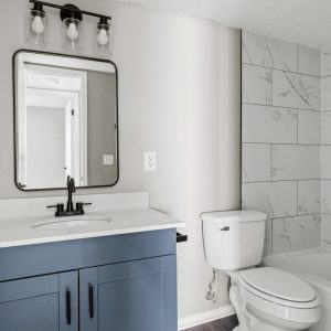 Renovated bathroom with blue vanity, black fixtures, and marble-tiled tub surround in a South Oklahoma City apartment.