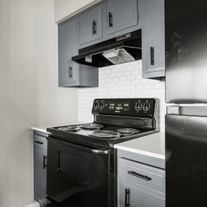 Renovated kitchen with black electric range, stovetop hood, subway tile backsplash, and gray cabinetry