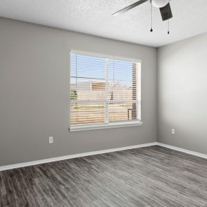 Empty renovated bedroom with gray walls, wood-look flooring, ceiling fan, and a large window with blinds
