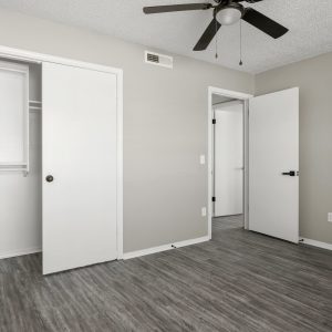 Empty renovated bedroom with sliding closet doors, ceiling fan, and gray wood-look flooring