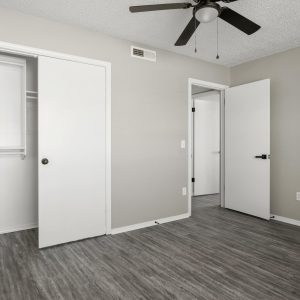 Empty renovated bedroom with sliding closet door, ceiling fan, and gray wood-look flooring